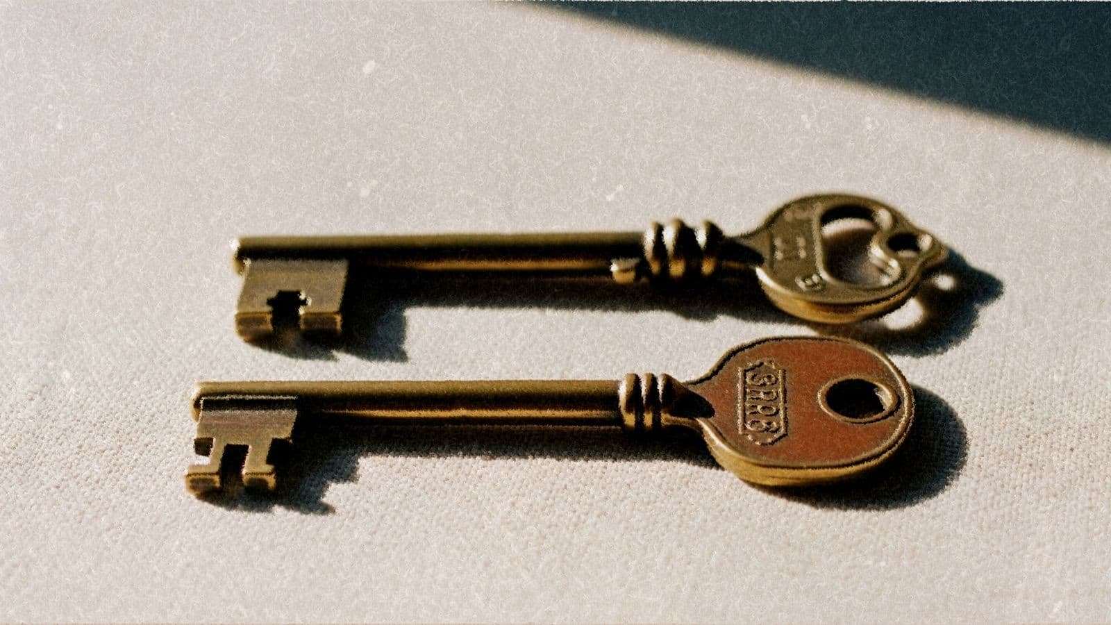 Two distinct vintage brass door keys side by side on cream linen.
