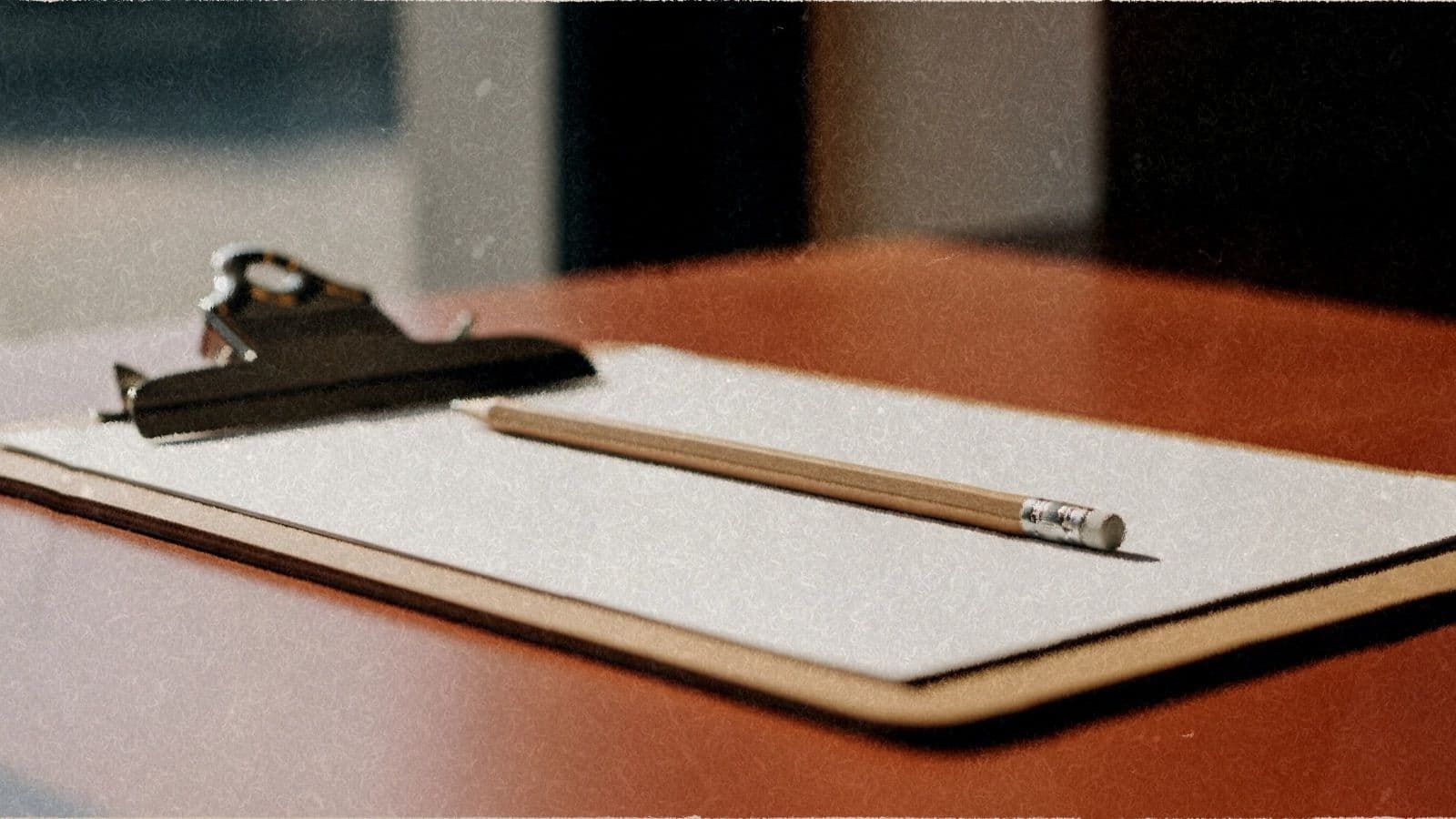 A wooden clipboard holding blank paper with a pencil, on a shop counter.