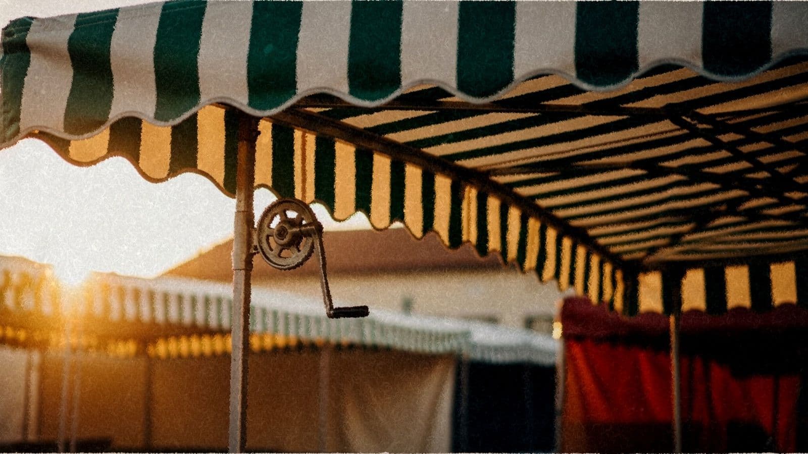 A green-striped market stall awning being cranked open at dawn.